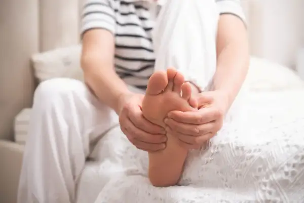 Osoba masuje stopę, odczuwając ból związany z neuropatią cukrzycową.