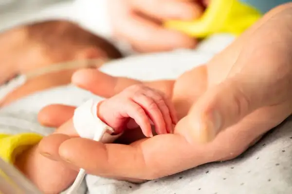 Dłoń rodzica obejmuje maleńką dłoń dziecka z zespołem Edwardsa, otoczoną troską i nadzieją.